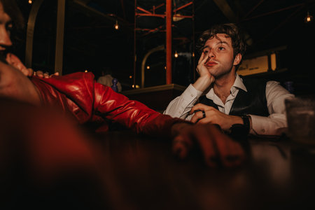 Young man in a vintage vest at a dimly lit bar, lost in thought during a night outの写真素材