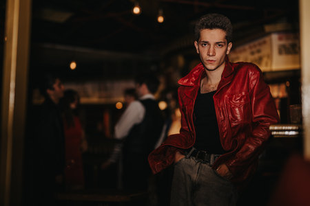 Confident man in a red leather jacket stands in a night club with an urban, moody vibeの写真素材