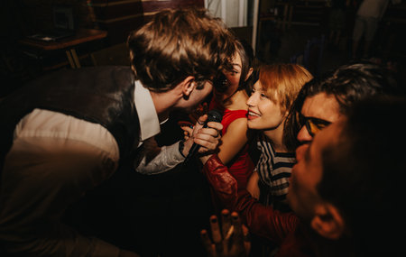 Friends sing along at a lively night out, sharing a microphone moment with laughter and energyの写真素材