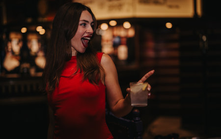 Joyful woman in red dress laughing during a night out with a drink in handの写真素材