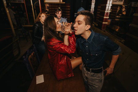 Friends enjoy a night out at a bar as a couple shares a kiss and drinkの写真素材