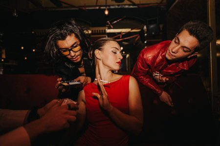 Night out with friends in a dim lounge as a woman in red dress poses with onlookersの写真素材