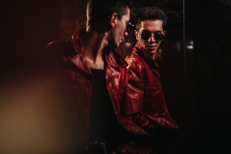 Man in red leather jacket looks at his reflection in a dark moody urban sceneの写真素材