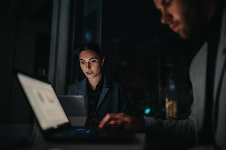 Focused business professional reviews data on a laptop in a modern office at nightの写真素材