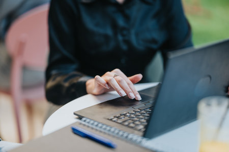 Person typing on a laptop at an outdoor cafe with notebook and penの写真素材