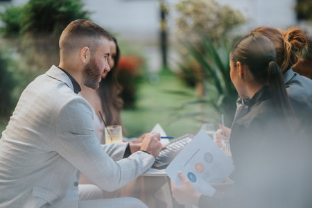 Business meeting outdoors with colleagues at a cafe, reviewing documents and laptop for collaborationの写真素材