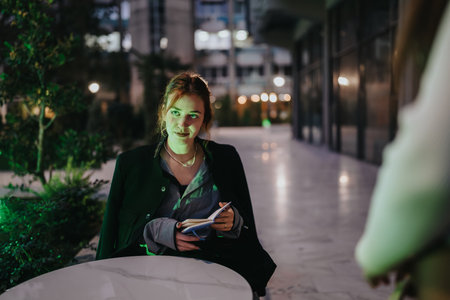 Confident woman at an outdoor night cafe with notebook in a modern urban settingの写真素材