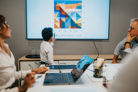 Young presenter leads a business meeting as colleagues watch a colorful chart on a large screen