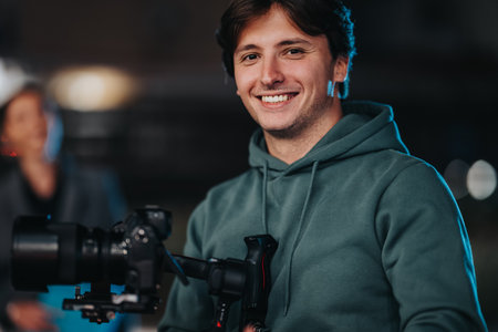 Smiling camera operator in teal hoodie with professional video rig during outdoor shootの写真素材
