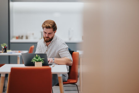 Business professional works on a laptop at a modern office desk with a small plant nearby
