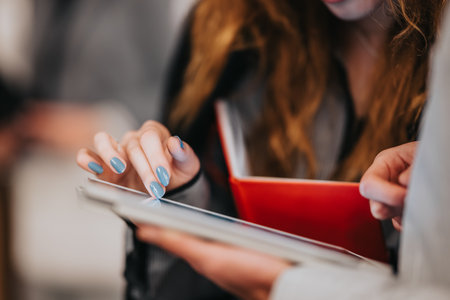 Two people collaborate over a tablet and a red notebook in a modern workspace