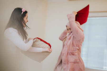Two girls playfully having a pillow fight in a cozy home settingの写真素材
