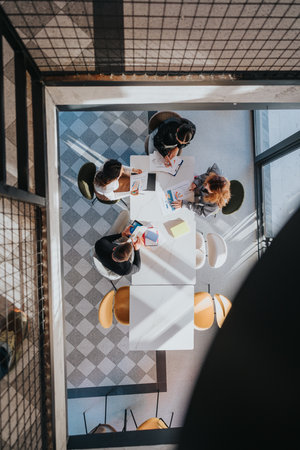 A collaborative business meeting around a white table with documents and charts in a modern office spaceの写真素材