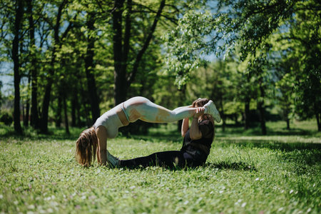Two women exercising outdoors practicing fitness postures in a sunny park settingの写真素材