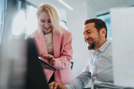 Collaborating colleagues discuss on laptop as a smiling professional woman assists at the office deskの写真素材