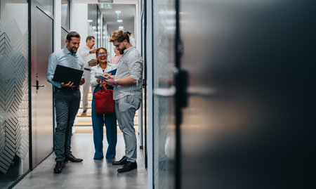 Team of professionals in a modern office hallway discussing documents and projects togetherの写真素材