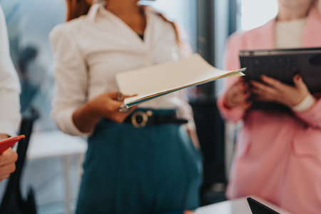 Business meeting with colleagues reviewing documents in a modern office setting, holding files and discussing projectsの写真素材