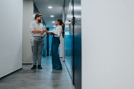 Professional handshake between colleagues in modern office hallway with documents and clipboardの写真素材
