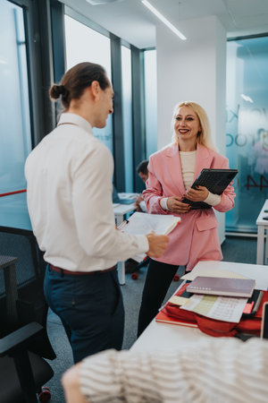 Business colleagues in a modern office chatting and sharing documents, pink blazer woman smilingの写真素材