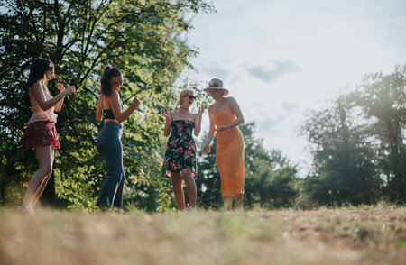 Four women enjoying a sunny day outdoors, dancing and laughing in a parkの写真素材