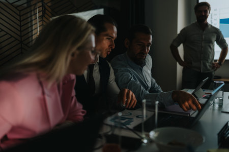 Business meeting among professionals in a dim office, focused on a laptop and chartsの写真素材