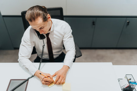 Busy office professional at a desk, talking on the phone, and jotting notesの写真素材