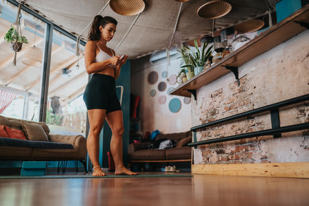 Woman practicing yoga in a cozy home studio, standing on a mat and using a smartphoneの写真素材