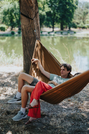 Two friends relax in a brown hammock by a sunny lakeside park on a warm afternoonの写真素材