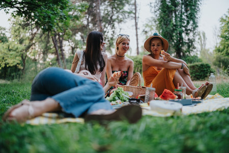 Friends enjoy a sunny park picnic together, sharing food, laughter, and a relaxing afternoon outdoorsの写真素材