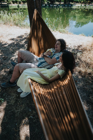 Couple relaxing in a hammock by a serene lake under shade trees and sunの写真素材