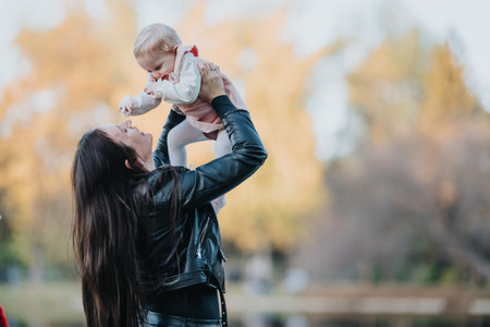 Mother lifts baby high in autumn park, joyful outdoor family momentの写真素材
