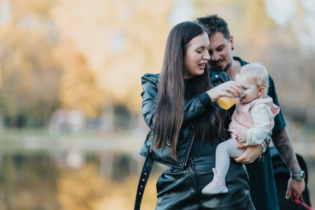 Family in an autumn park: mother feeds baby as father smiles, capturing warm, playful momentの写真素材