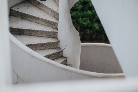 Spiral concrete staircase curves outdoors beside a white wall with greenery in the backgroundの写真素材