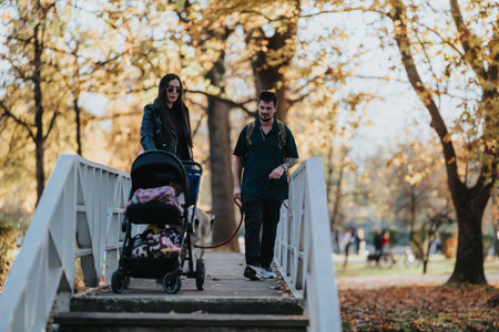 Couple walks on a white railing bridge with a stroller and dog through an autumn park settingの写真素材