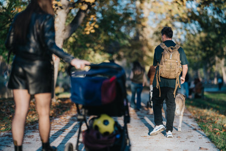 Man with backpack walks a dog in autumn park as a woman pushes a stroller nearbyの写真素材