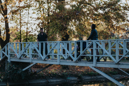Families and friends cross a white wooden bridge in an autumn park settingの写真素材