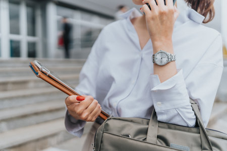 Close-up of a business person holding documents and talking on a smartphoneの写真素材