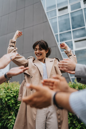 Woman celebrating achievement surrounded by supportive hands outdoorsの写真素材