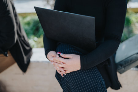 Young professional outdoors with a laptop, hands clasped, creating a casual business vibeの写真素材