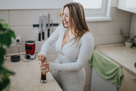 Woman smiling and preparing a drink in a cozy kitchenの写真素材