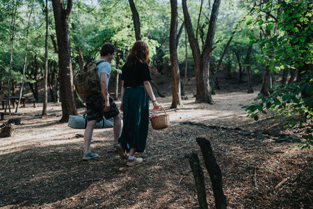Friends explore a sunlit forest path with a picnic basket on a relaxed outdoors dayの写真素材