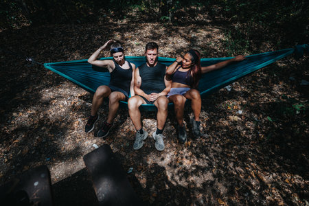 Friends relax in a blue hammock during an outdoor forest camping trip