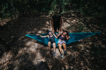 Friends in a blue hammock enjoying an outdoor forest camping and teamworkの写真素材