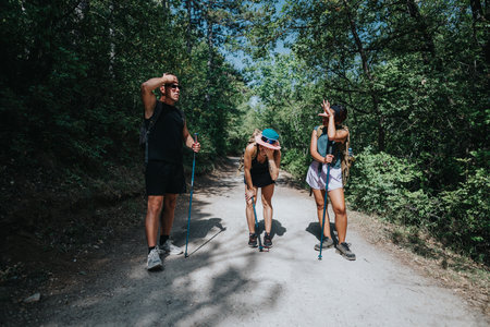 Three hikers on a sunlit forest trail with trekking poles during a group outdoor hikeの写真素材