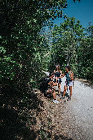 Three hikers pause on a sunlit forest trail during an outdoor hike with backpacks and trekking polesの写真素材