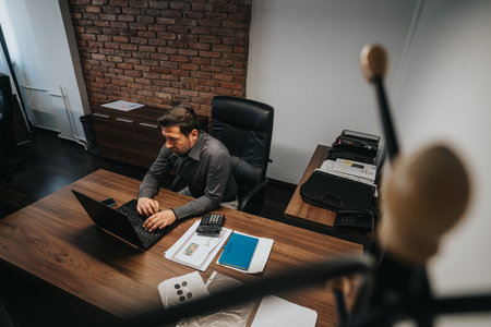 Businessman working on laptop at desk in a modern office settingの写真素材