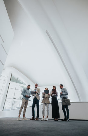 Group of colleagues in a bright modern atrium collaborating on tablets and documentsの写真素材