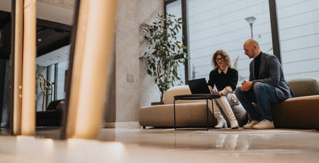 Business partners discuss on a laptop in a modern lobby lounge settingの写真素材