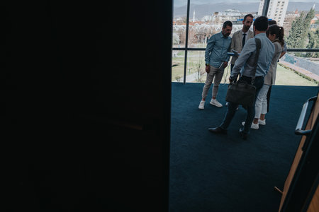 Group of colleagues discussing a project in a modern office lobby by large windowsの写真素材