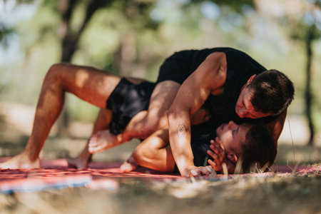 Two men wrestle on a mat outdoors in a sunny park during a casual workoutの写真素材